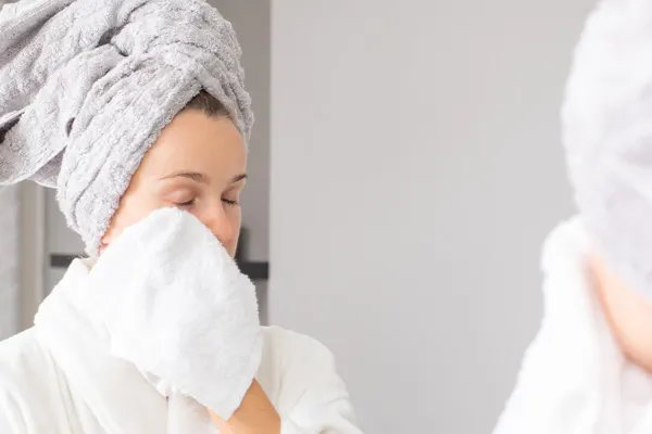 Kobieta po oczyszczaniu twarzy wyciera twarz bawełnianym ręcznikiem